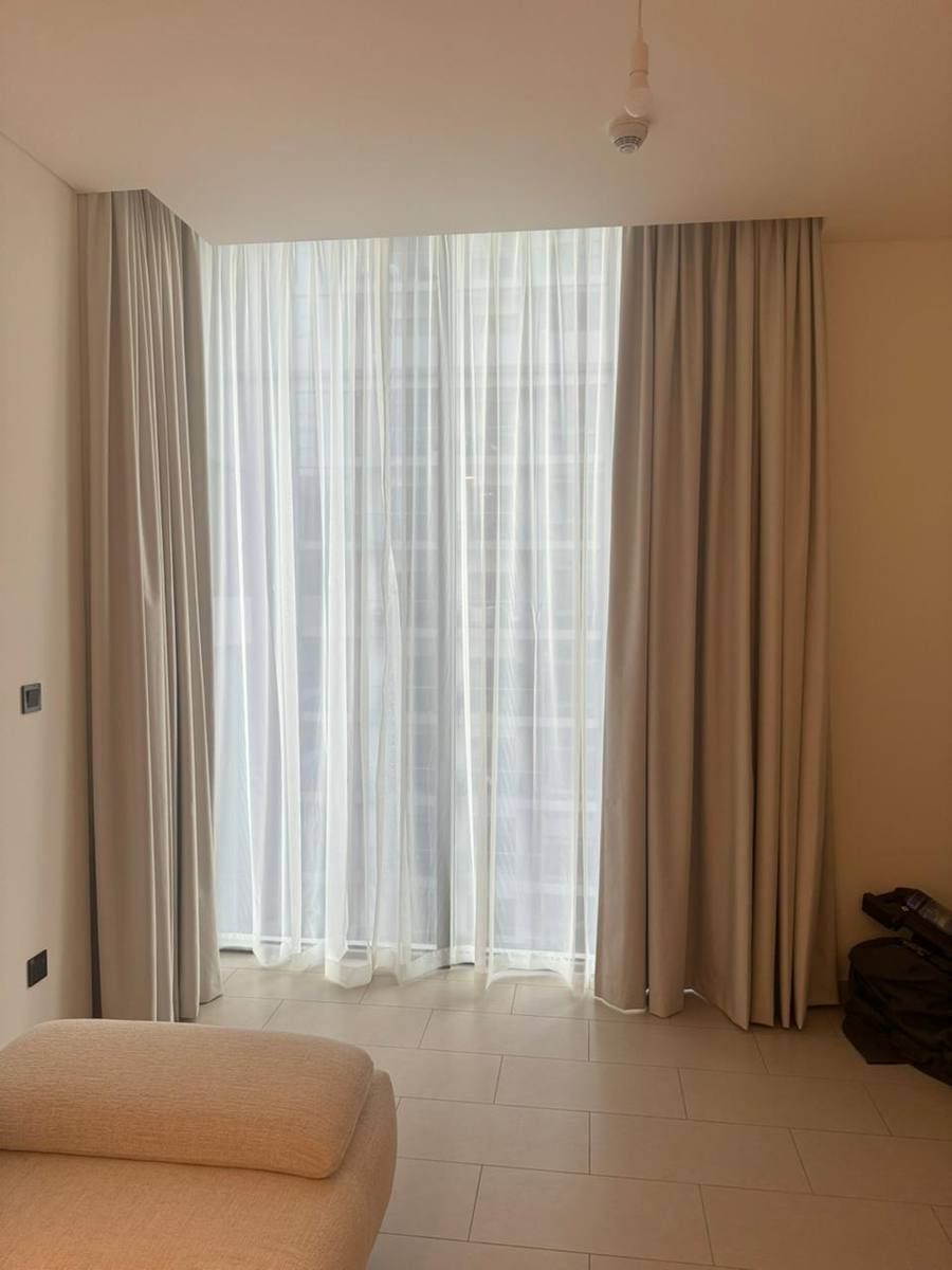 Cream sheers and curtains wrapping a corner window beside an armchair