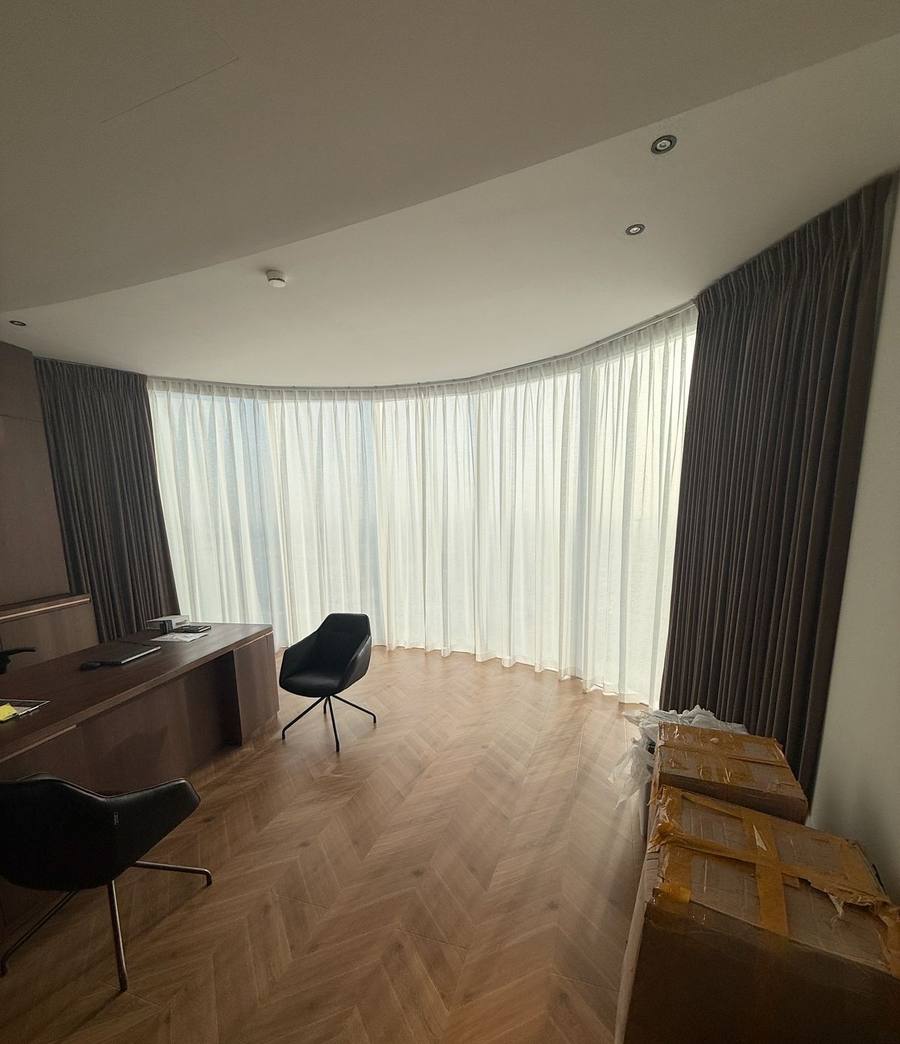 Grey wave curtains and sheers following a curved bay window over herringbone flooring