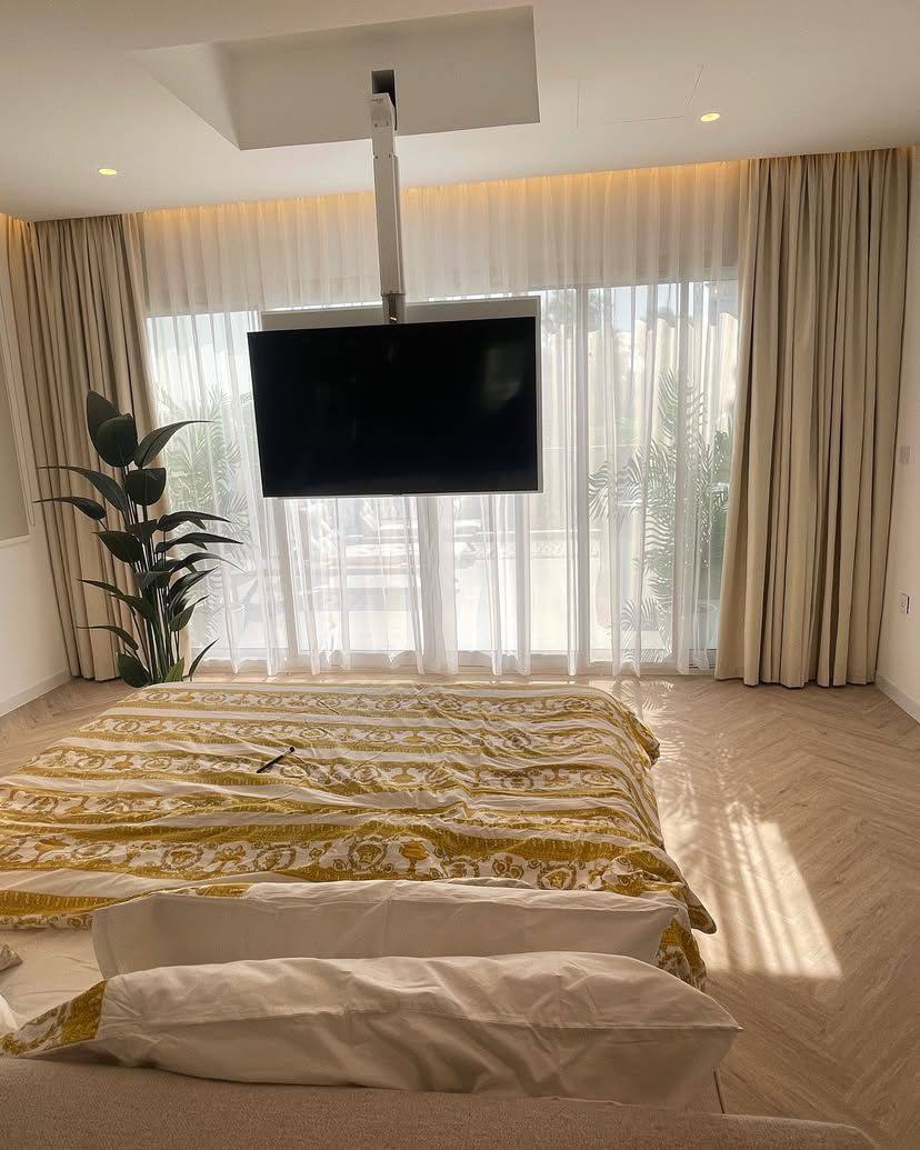 Sheer curtains installed behind a ceiling-mounted television in a bedroom