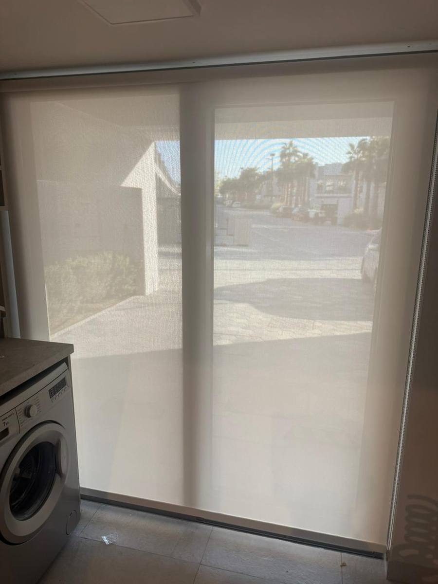 Sunscreen roller blind covering a wide sliding door in a utility area